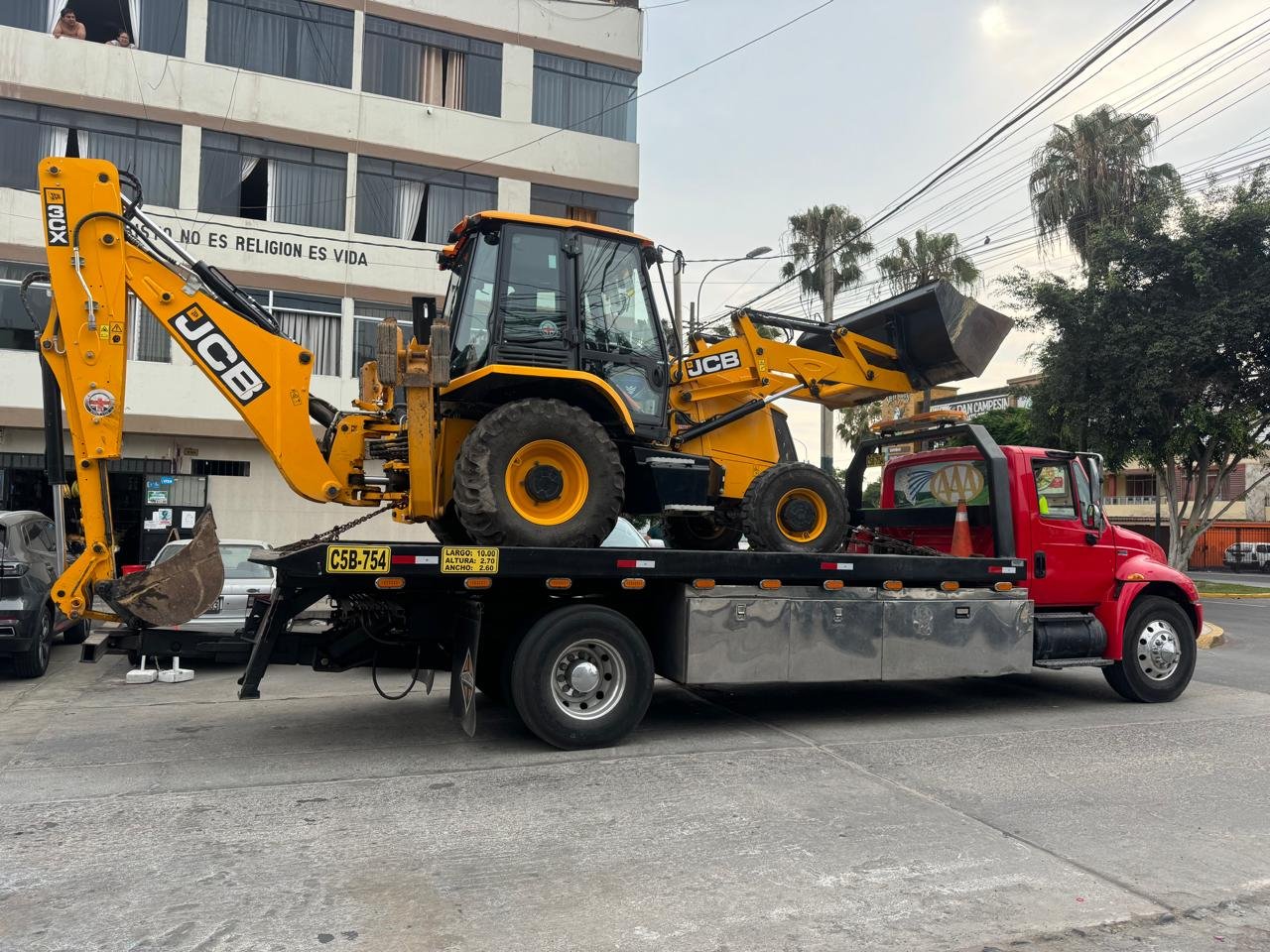 Grúa plataforma trasladando una retroexcavadora JCB 3CX