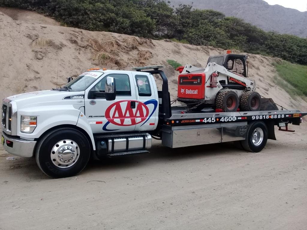 Grúa plataforma trasladando un minicargador Bobcat