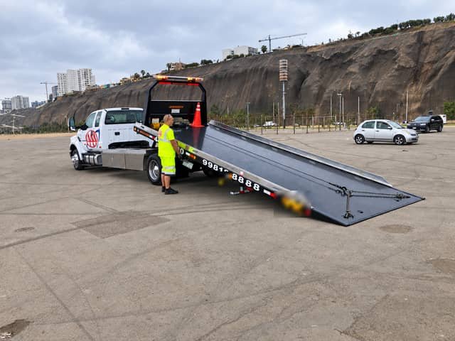 Operador de Grúas Triple A con chaleco reflectivo junto a una grúa plataforma F-650 con la rampa abajo