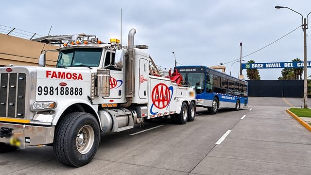 Grúa pesada remolcando un bus interprovincial azul por una avenida